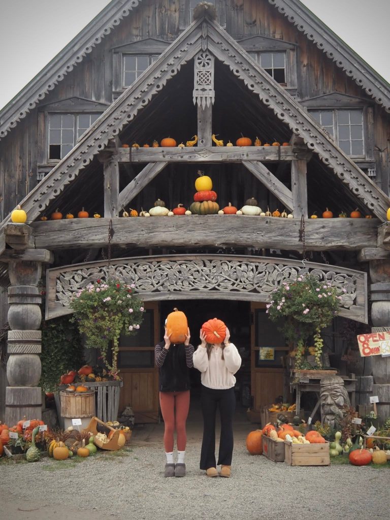 Two Girls standing in front of a weathered building with pumpkins in front of their faces