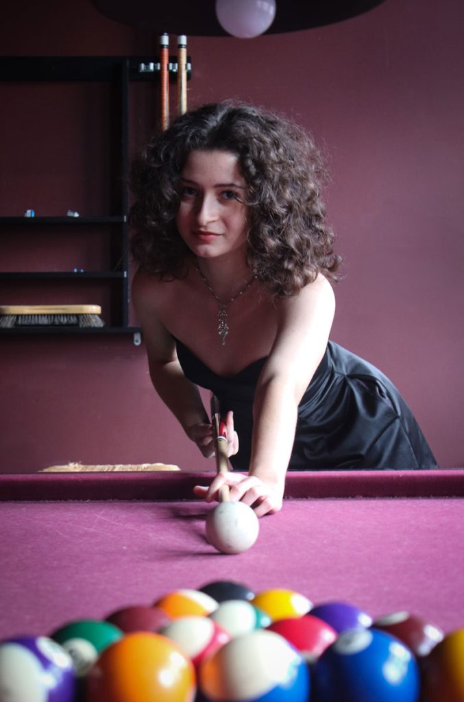 Teen in a black dress playing pool